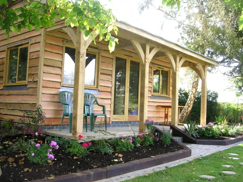 A picturesque oak frame garden room with a covered veranda, nestled in a lush garden setting.