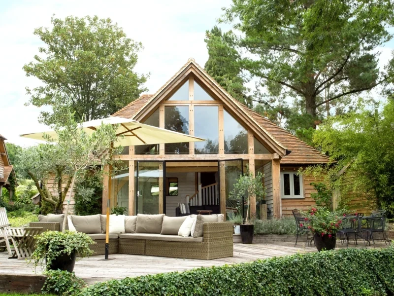 A modern oak frame garden annexe with a vaulted ceiling and large glazed gable end, opening onto a spacious patio area with outdoor seating.