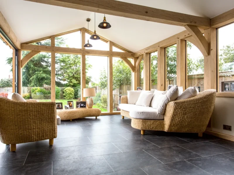 Spacious oak building project, an oak frame garden room with large windows, a vaulted ceiling with exposed beams, and comfortable wicker furniture.