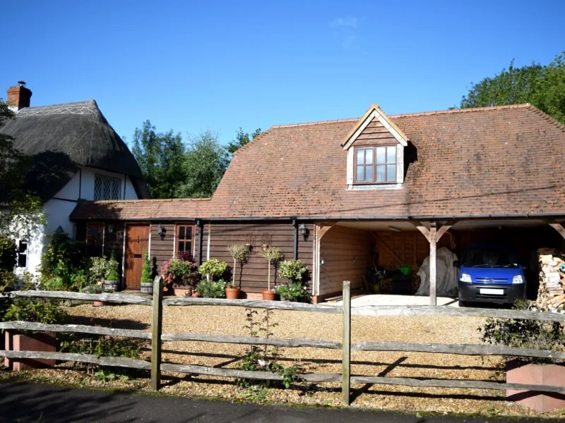 A charming oak frame building with a garage, carport, and upstairs living space, set in a picturesque countryside location.