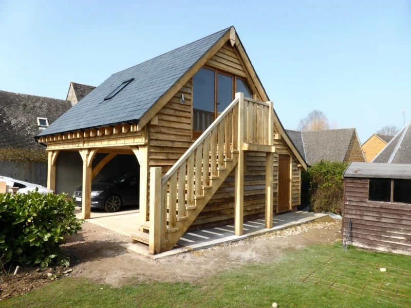 A beautiful oak frame garage with an upper floor accessed by an external oak staircase, featuring ledge and brace doors.