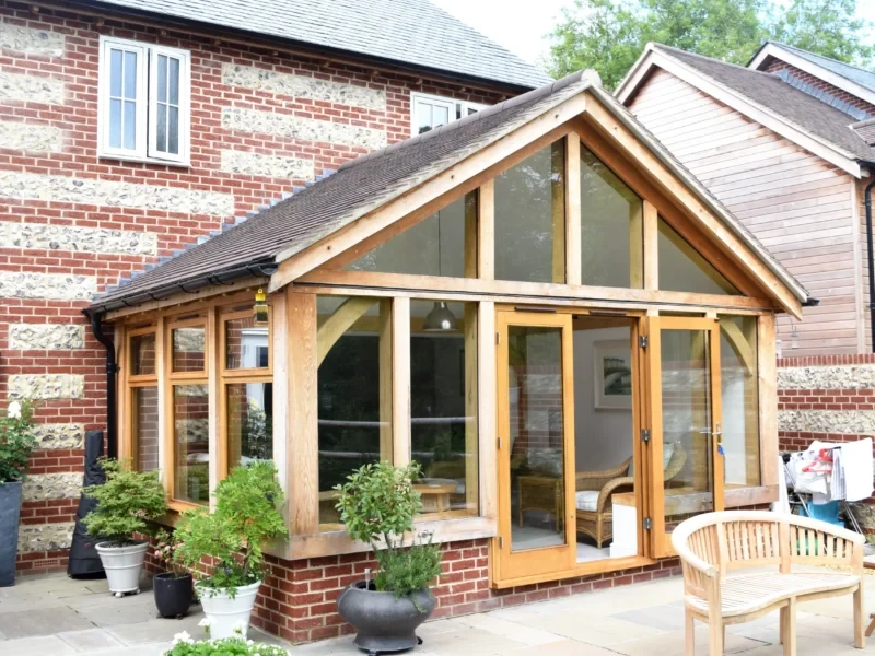 A modern oak framed extension with a vaulted ceiling and bi-fold doors leading to a patio. The extension is attached to a brick house and features large windows.