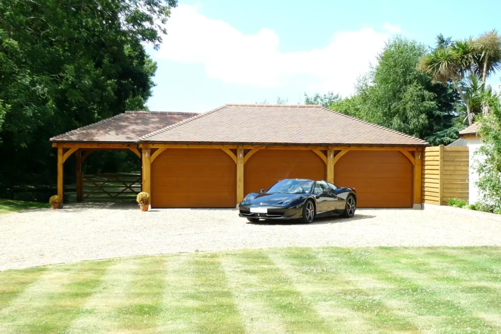 A classic four bay oak framed garage by oakcraft. A black sports car is parked on the gravel driveway.