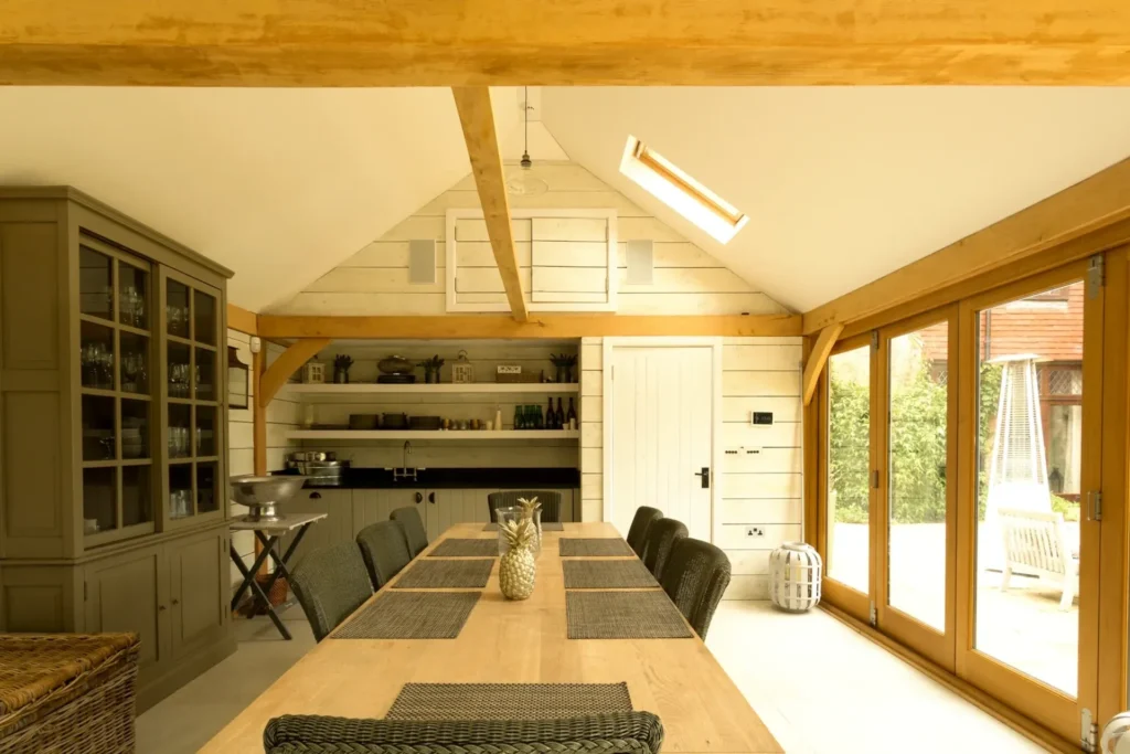 Interior of a spacious oak framed annexe featuring a vaulted ceiling, exposed beams, and french doors leading to a patio.