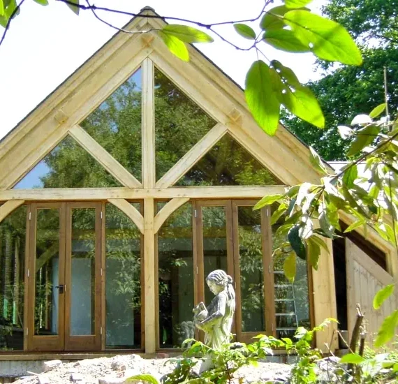 Oak framed extension with glazed gable end featuring traditional timber frame construction and full-height windows against brick house.