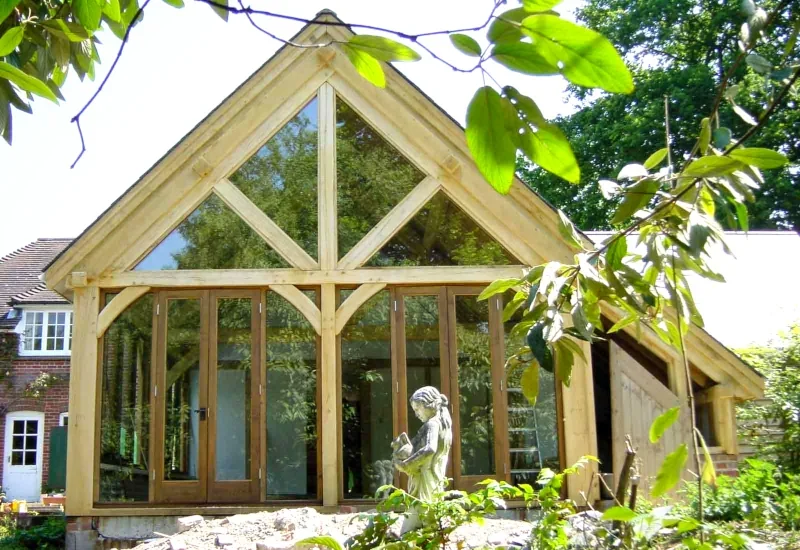 Oak framed extension with glazed gable end featuring traditional timber frame construction and full-height windows against brick house.