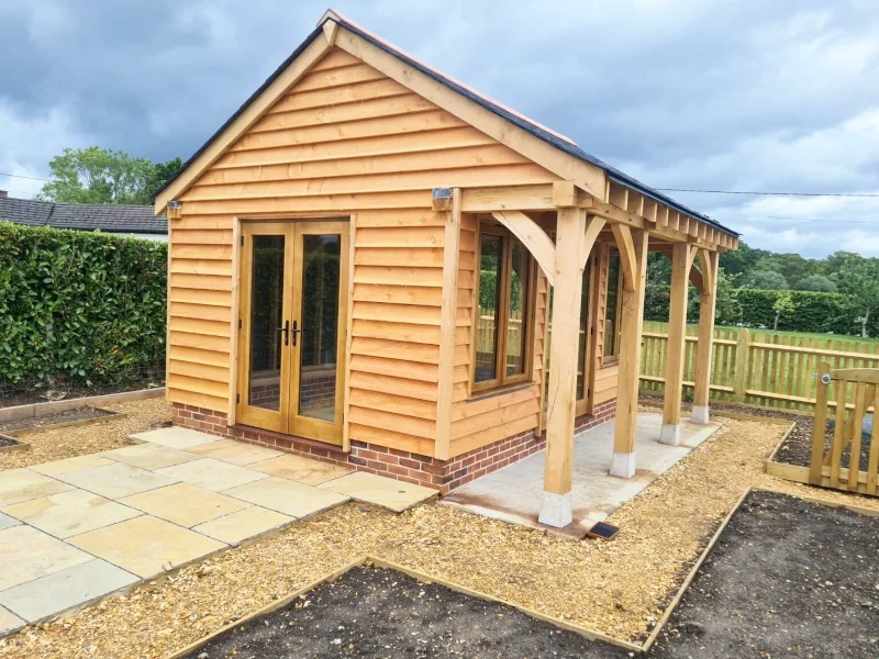 Light-filled bespoke oak-framed garden annexe with french doors and covered veranda, ideal for an artist's studio or creative workspace.