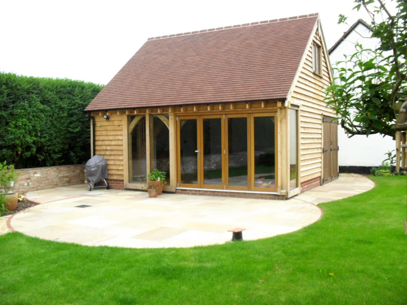 Spacious bespoke oak-framed garden annexe with bi-fold doors and curved patio, perfect for a teen hangout or children's playroom.