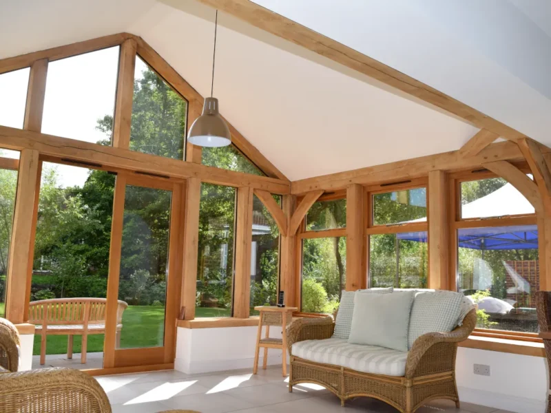 Bespoke oak framed building in Dorset featuring handcrafted oak frame, vaulted ceiling with exposed beams, floor-to-ceiling windows, and luxury garden room furnishings