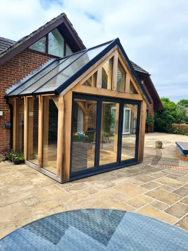 Bespoke oak framed buildings in berkshire showcasing a glazed garden room extension with glass roof lantern and contemporary bifold doors on natural stone patio