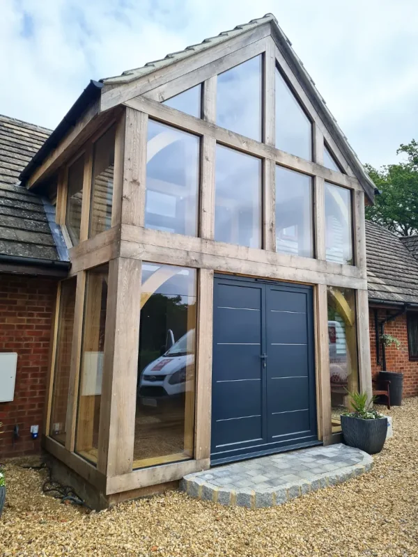 Bespoke oak framed buildings in berkshire featuring a double-height glazed entrance with contemporary grey doors and traditional oak frame construction