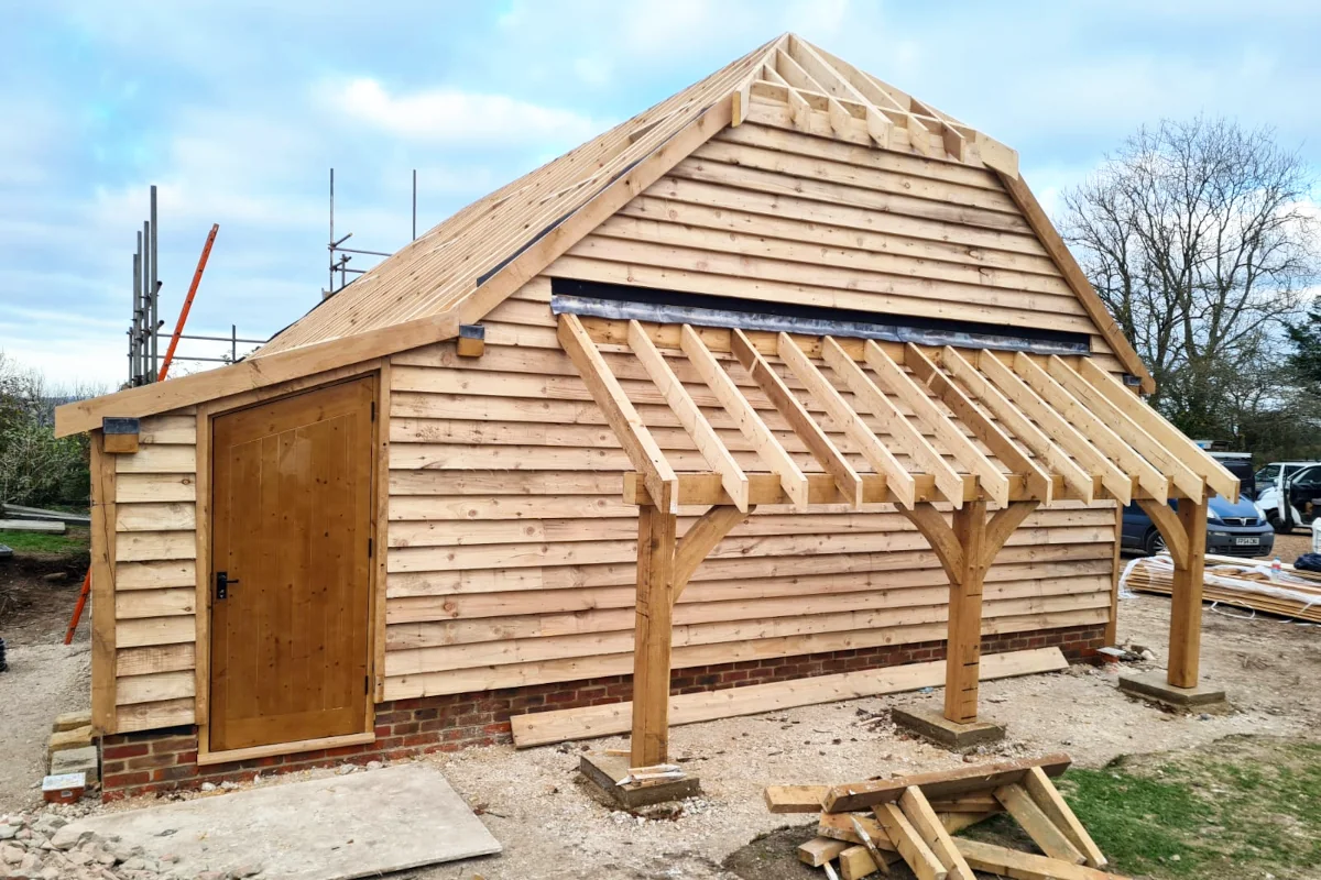 Three-bay oak frame garage with log store under construction in salisbury, wiltshire