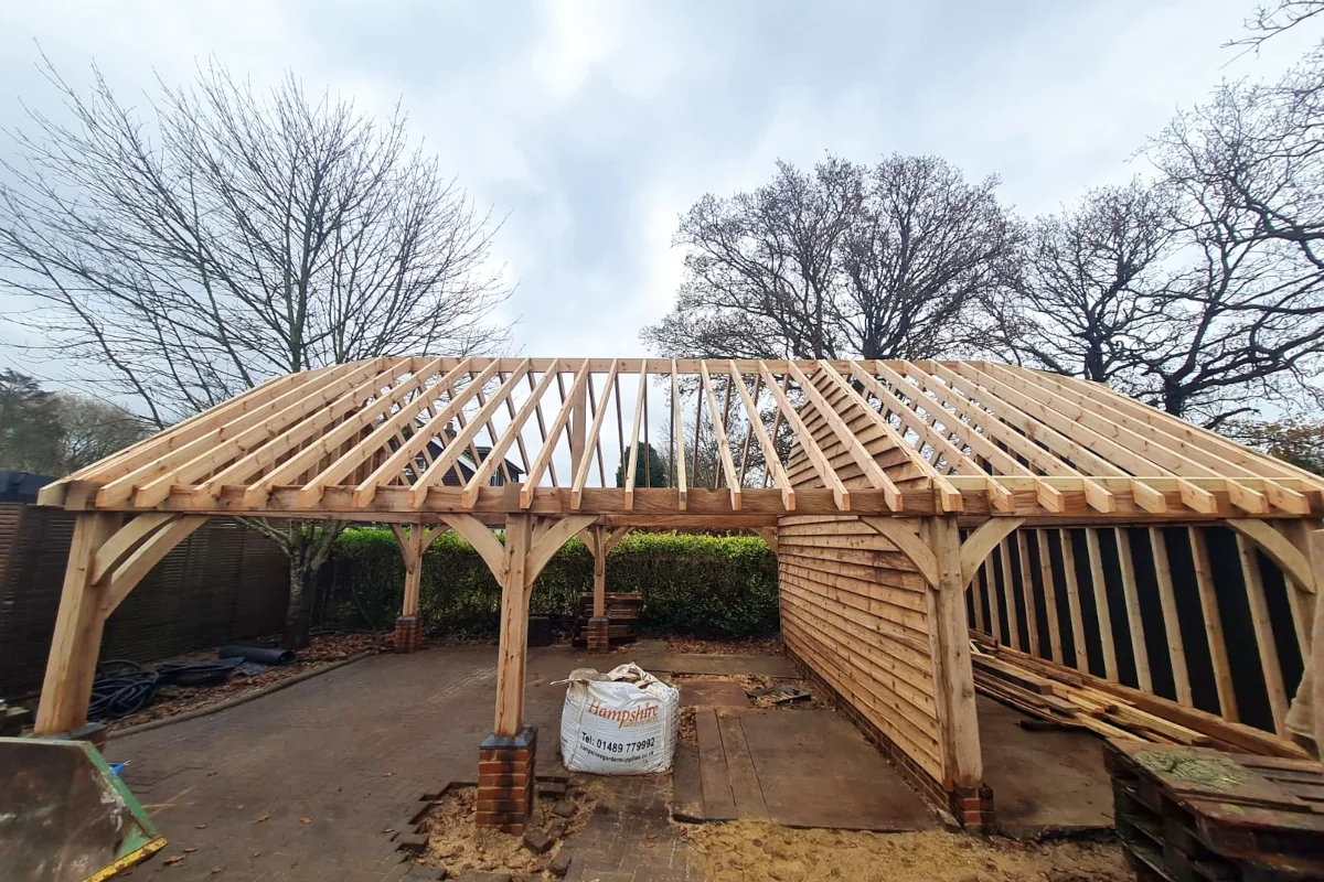 Newly completed three-bay oak frame garage structure in warsash showing traditional craftsmanship with cropped hip roof trusses and handcrafted oak posts