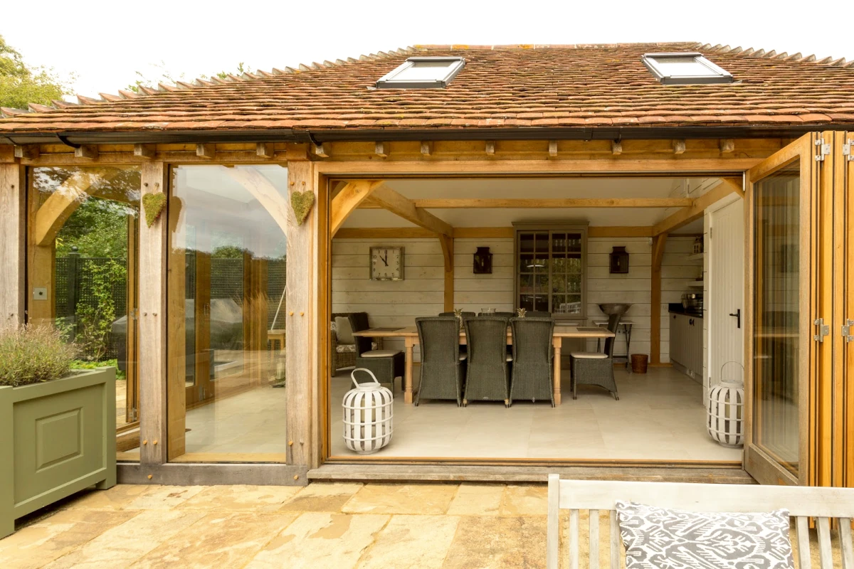 Interior view of oak frame annexe showing open-plan dining area with bifold doors, exposed oak beams, and contemporary country furniture