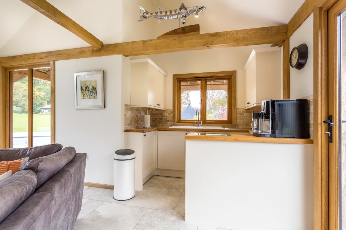 Open plan kitchen and living area in oak frame annexe featuring exposed beams, cream shaker units, oak worktops and limestone flooring with garden views