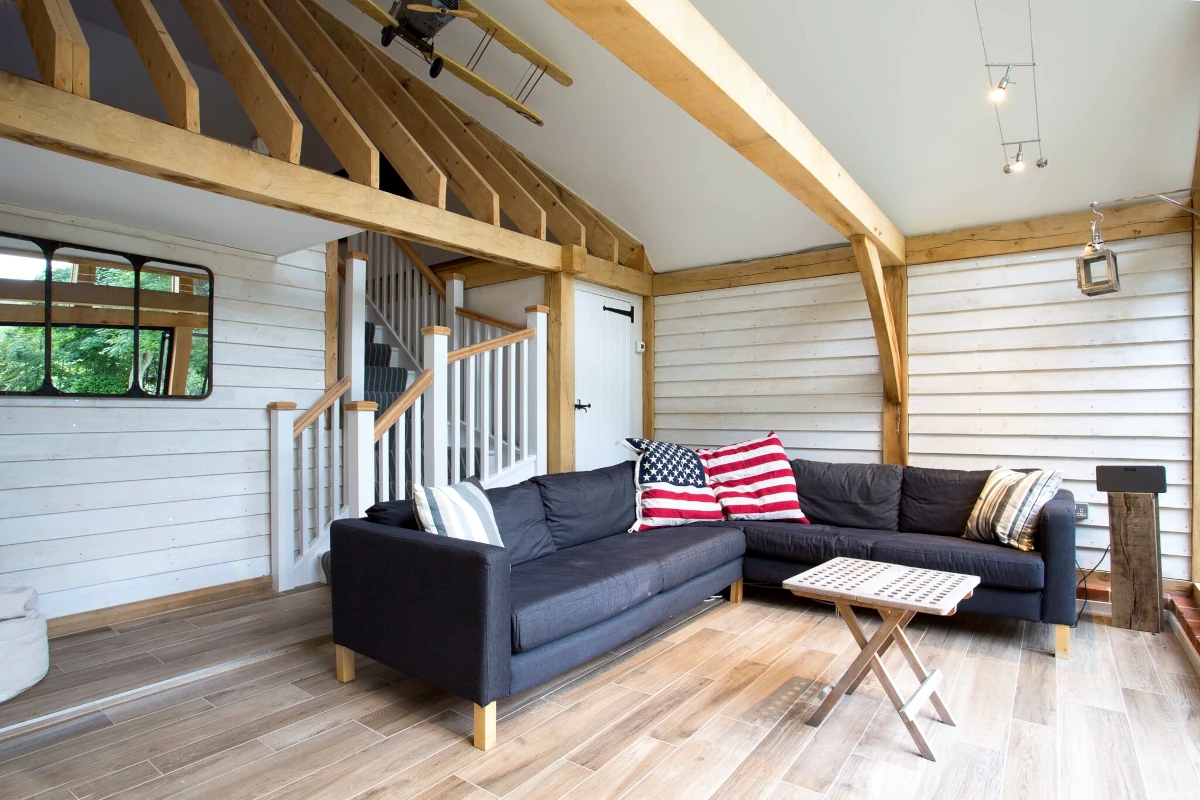 Modern oak frame annexe living room featuring exposed beams, painted cladding, mezzanine level and contemporary grey corner sofa with wood-effect flooring