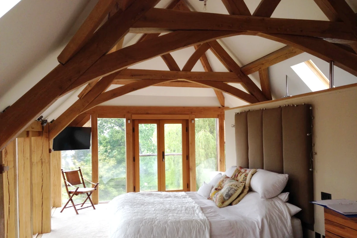 Vaulted bedroom with exposed oak trusses and natural light, featuring handcrafted timber frame construction in traditional british style