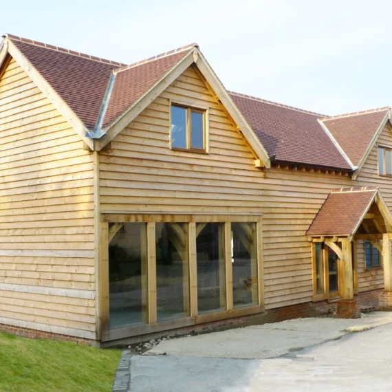 Oak frame construction detached building with timber cladding, floor-to-ceiling glazing, dormers and traditional oak frame porch design showcasing british craftsmanship