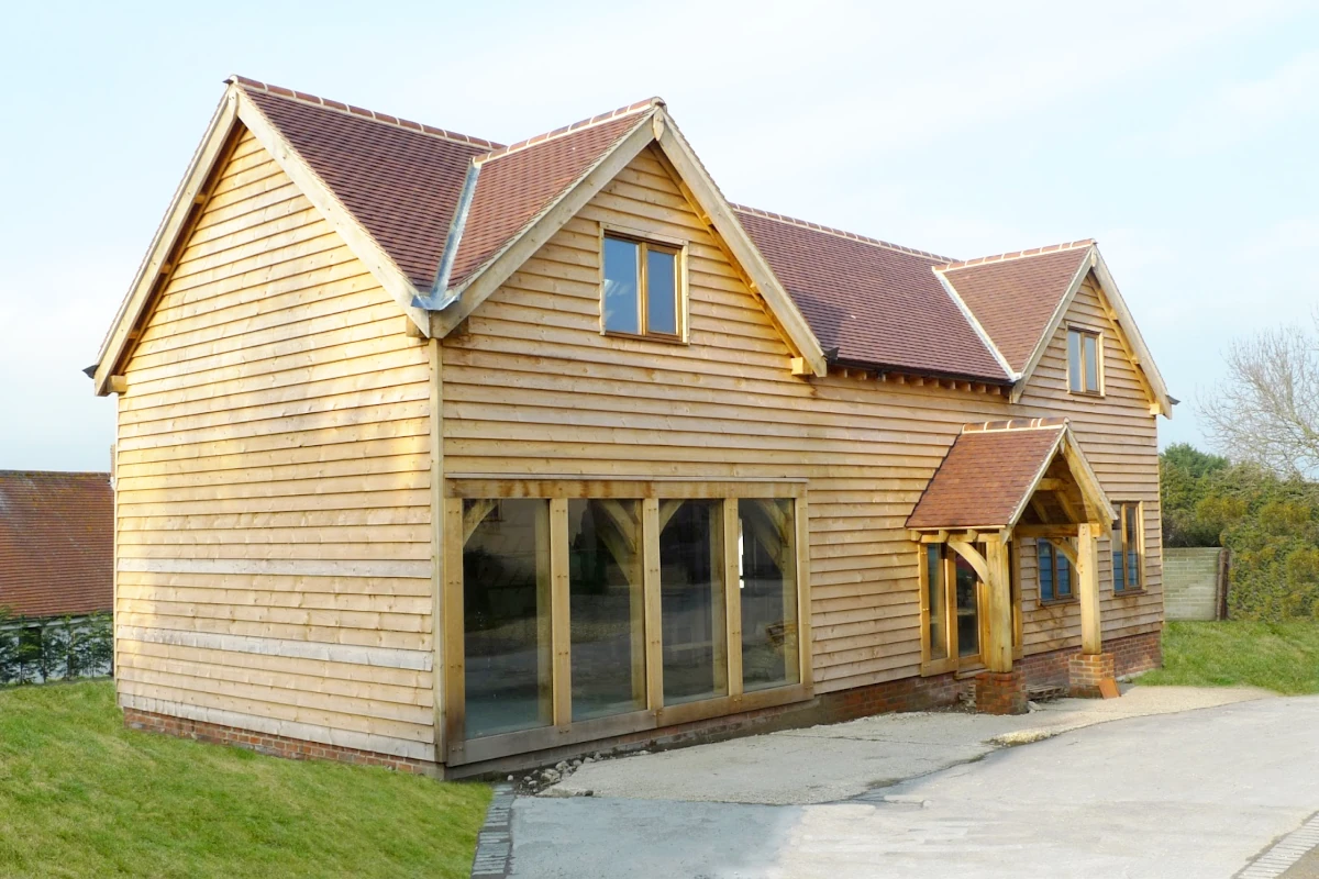 Oak frame construction detached building with timber cladding, floor-to-ceiling glazing, dormers and traditional oak frame porch design showcasing british craftsmanship