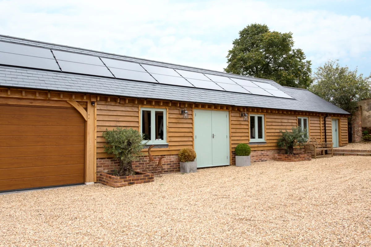 Oak frame construction project showing garage and annexe with integrated solar panels, cedar cladding, brick plinth, and modern features including timber garage door and sustainable design elements