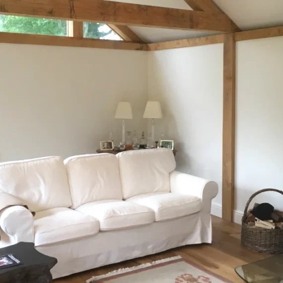 Modern oak frame living room featuring exposed beams, wood burning stove, white sofa and vaulted ceiling with garden views through feature windows