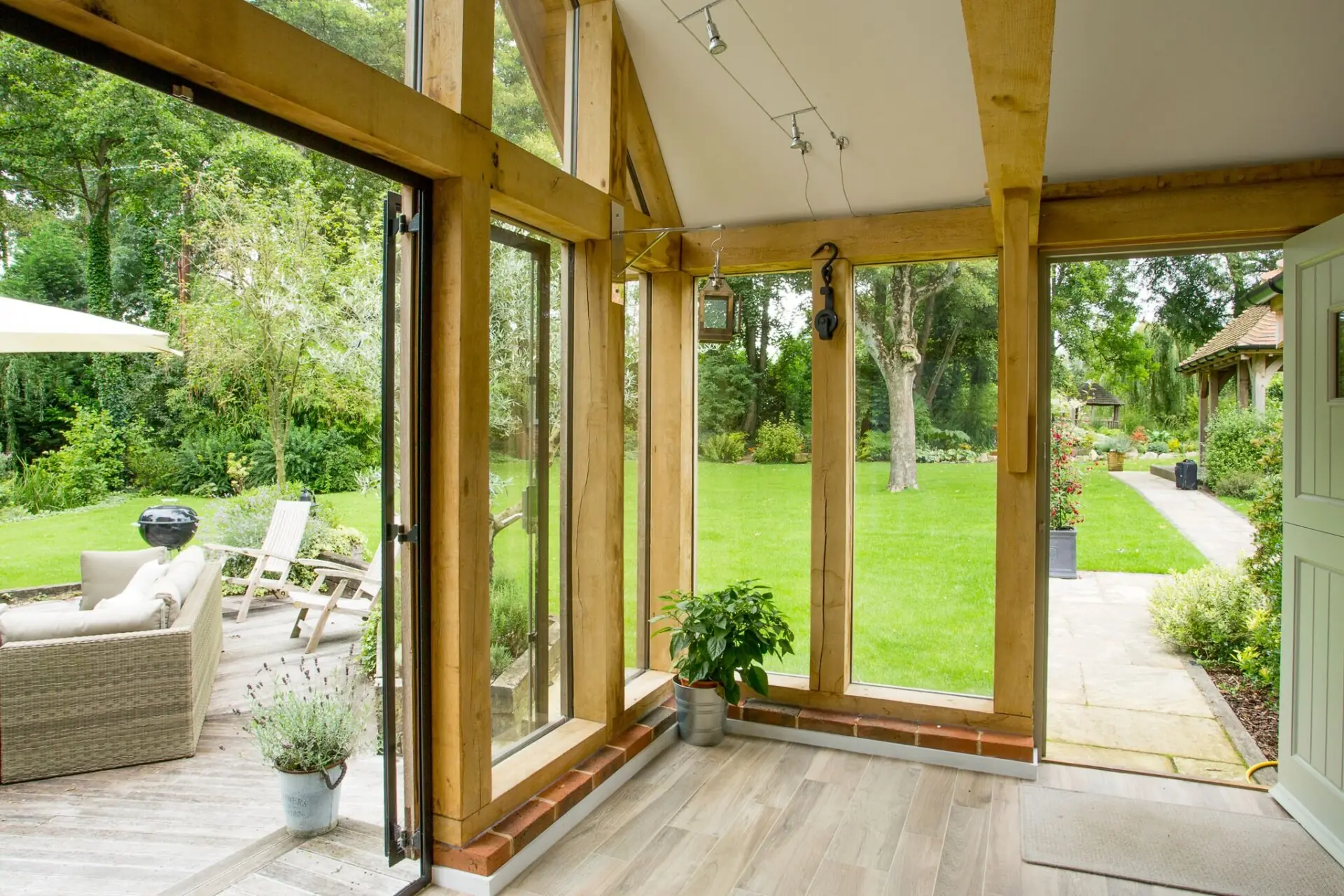 Interior detail of bespoke oak framed garden room showing handcrafted posts and beams, engineered oak flooring, and floor-to-ceiling glazing overlooking landscaped garden