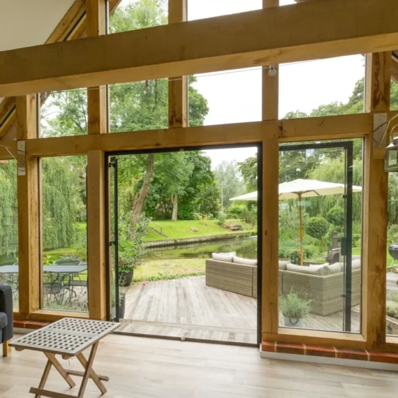 Bespoke oak framed building interior showing handcrafted beams, vaulted ceiling and architectural glazing overlooking landscaped garden with traditional ironwork lanterns