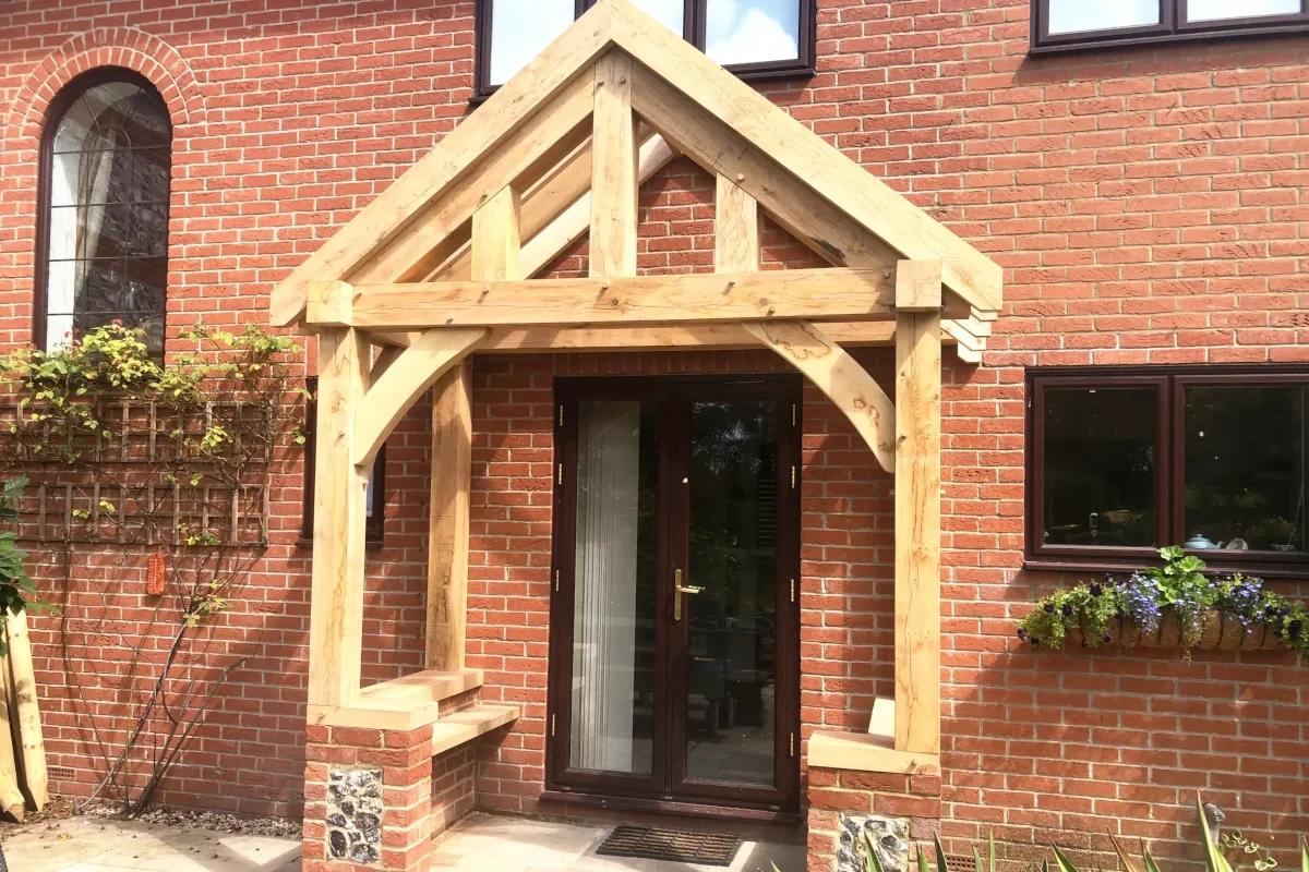 Traditional oak frame porch with king post truss and curved braces, featuring brick pillars and flint detail in Hampshire