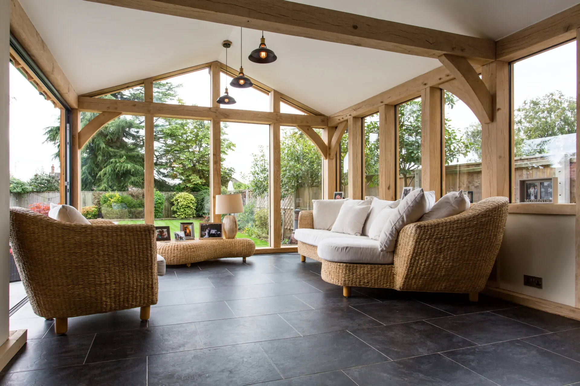 Oak framed home extension featuring handcrafted posts and braces, vaulted ceiling with exposed beams, and full-width bifold doors overlooking a mature garden