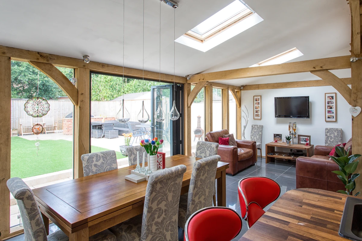 Bright oak-framed garden room extension featuring dining area, living space, bi-fold doors, skylights and artificial lawn garden view