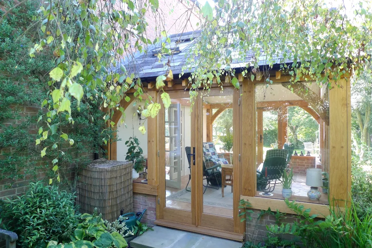 Bespoke oak framed garden room featuring full-height glazed panels, timber frame construction, and pitched roof, surrounded by mature garden planting