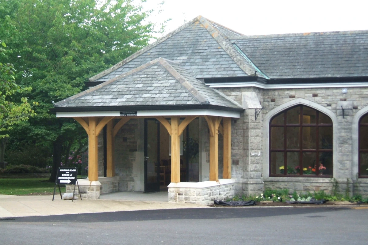 Oak framed porch entrance featuring natural posts, stone dwarf walls and Welsh slate roof, attached to traditional stone building with Gothic windows