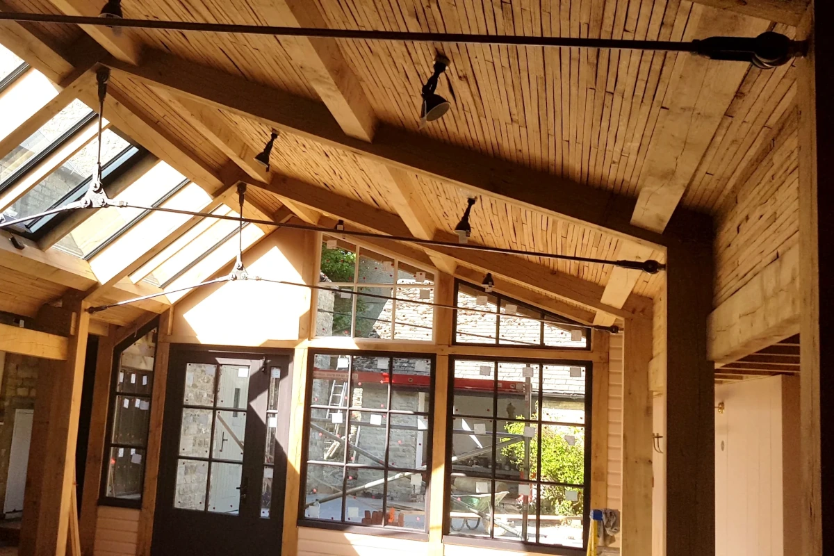 Interior view of oak roof structure featuring exposed trusses, multiple skylights, and industrial-style glazed doors bathed in natural light