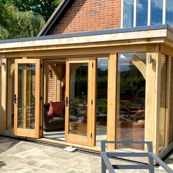 Modern oak-framed orangery featuring full-width bi-fold doors, york stone paving and brick detailing, showcasing contemporary orangery design in hampshire