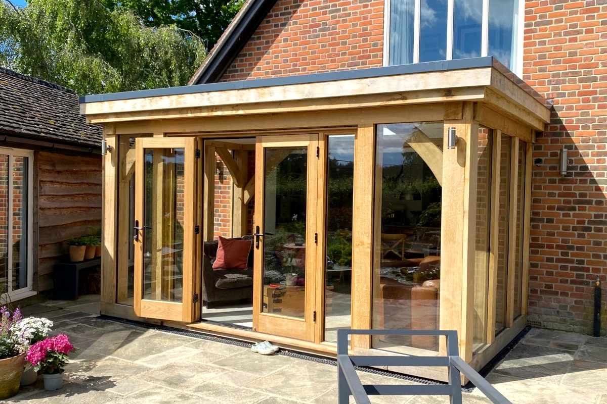 Modern oak-framed orangery featuring full-width bi-fold doors, york stone paving and brick detailing, showcasing contemporary orangery design in hampshire