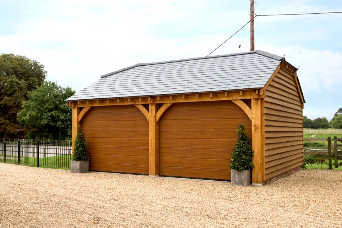 A well-built double oak garage with stunning cedar cladded doors. Our oak outbuildings can provide secure parking and enhance the kerb appeal of your UK property. The oak frame complements the surrounding landscape, and ads a touch of rustic charm.