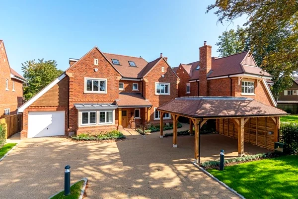 A stylish attached oak carport seamlessly integrated with a red brick house in the UK, providing sheltered parking and enhancing the property's kerb appeal. Our oak outbuildings can be designed to complement the architectural style of your existing home.