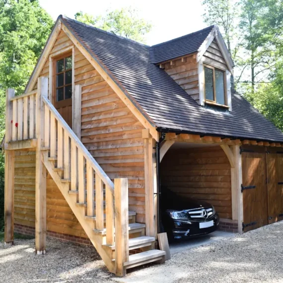 Stunning upper floored oak outbuilding, a bespoke oak framed double garage with loft accommodation, wooden staircase and traditional timber doors surrounded by mature trees in the British countryside