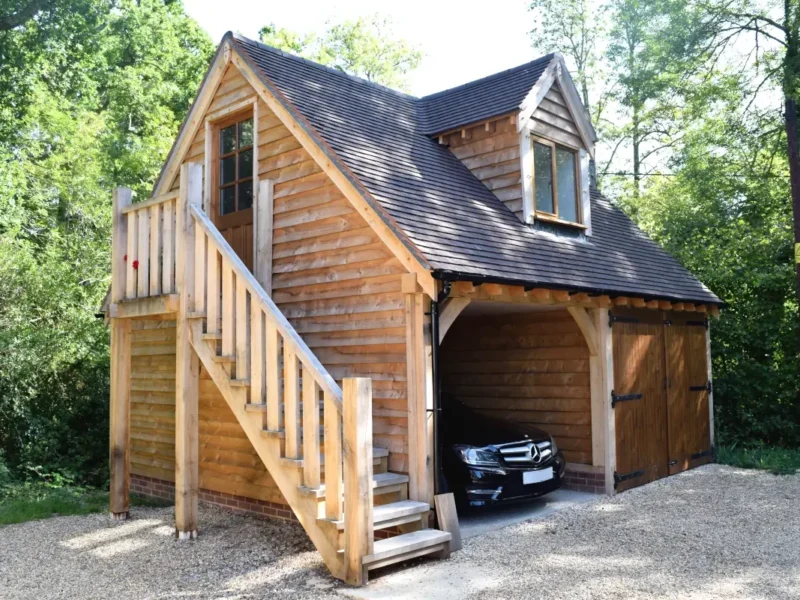 Stunning upper floored oak outbuilding, a bespoke oak framed double garage with loft accommodation, wooden staircase and traditional timber doors surrounded by mature trees in the British countryside