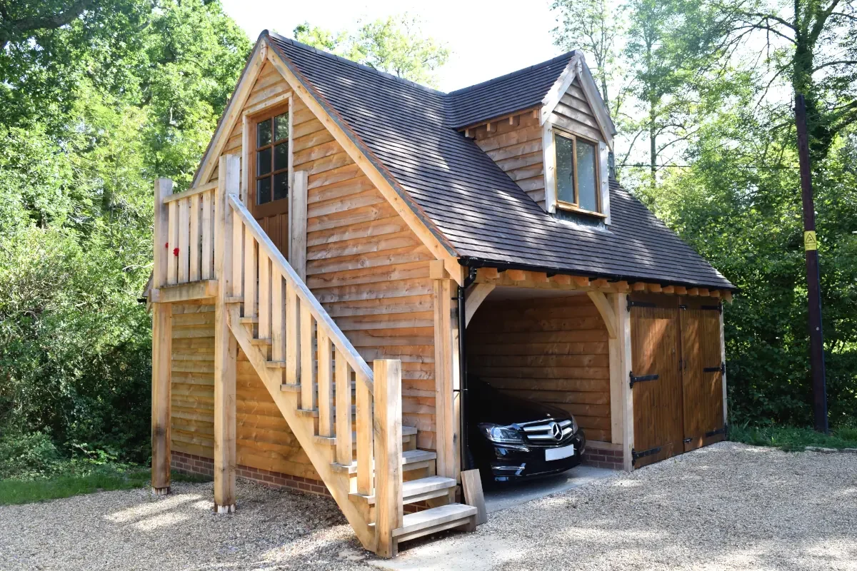 Stunning upper floored oak outbuilding, a bespoke oak framed double garage with loft accommodation, wooden staircase and traditional timber doors surrounded by mature trees in the British countryside