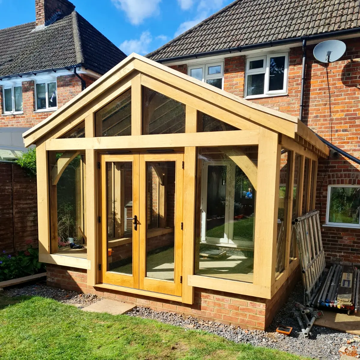 Compact oak framed garden room extension featuring full-height glazing, exposed oak frame and gable end design, built onto brick property