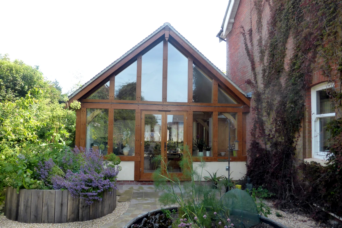 Oak framed garden room extension with full-height gable glazing, exposed oak frame and landscaped garden featuring natural planting