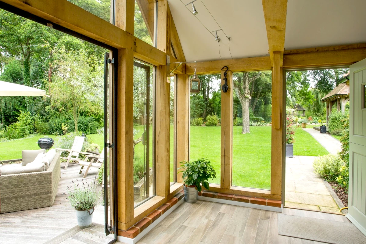 Light-filled oak framed garden room extension with floor-to-ceiling glazing, exposed oak posts and beams, overlooking landscaped garden