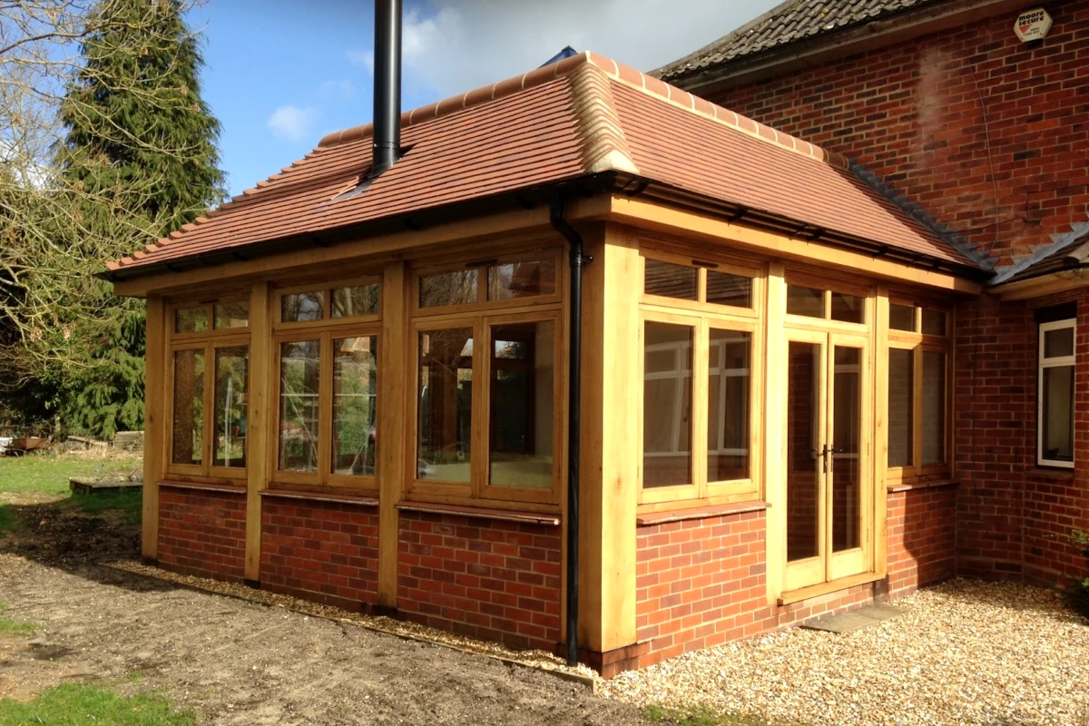 Bespoke oak-framed orangery featuring red brick base, clay tile roof and hardwood windows, built as an extension to a traditional hampshire home