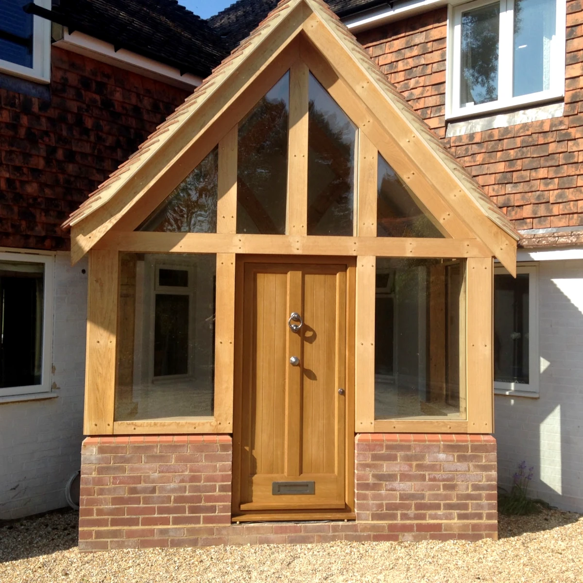 Oak framed porch with glazed gable end, solid oak door and handmade brick plinth adding character to this home entrance, oak framing from our hampshire workshop