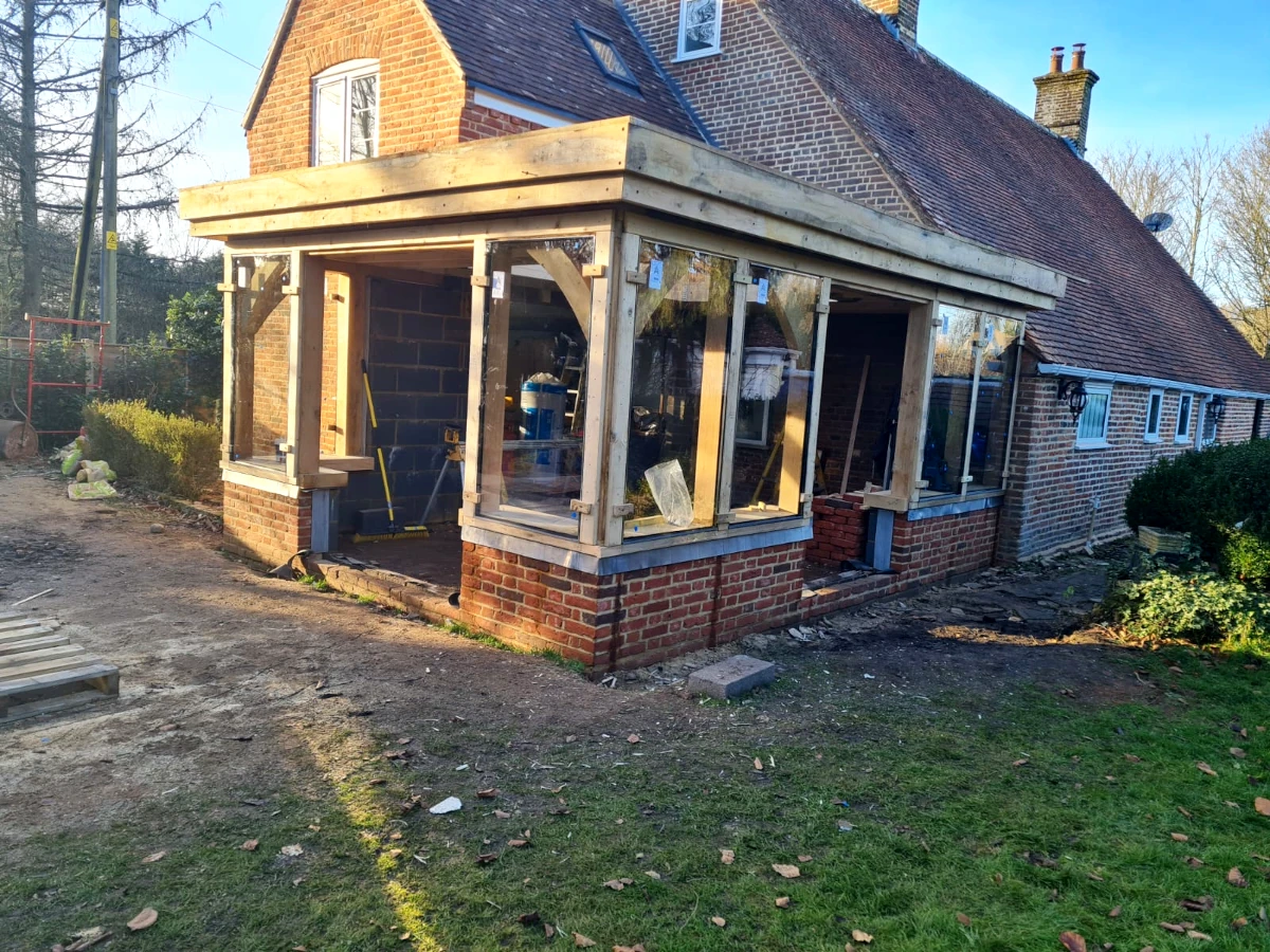 Oak framed orangery showing direct glazing installation phase with traditional brick base and oak posts in blashford, hampshire