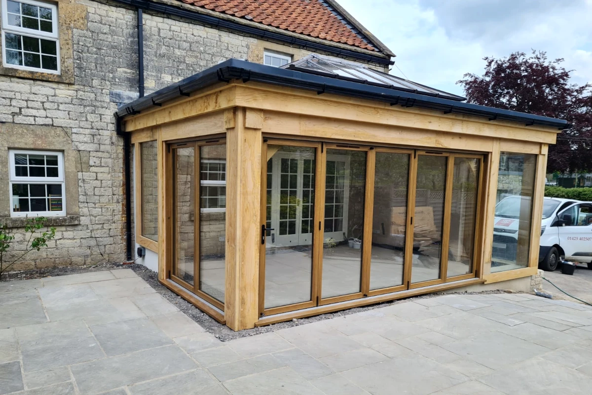 Traditional oak orangery with sliding glass doors and limestone paving, beautifully complementing a period stone cottage in hampshire