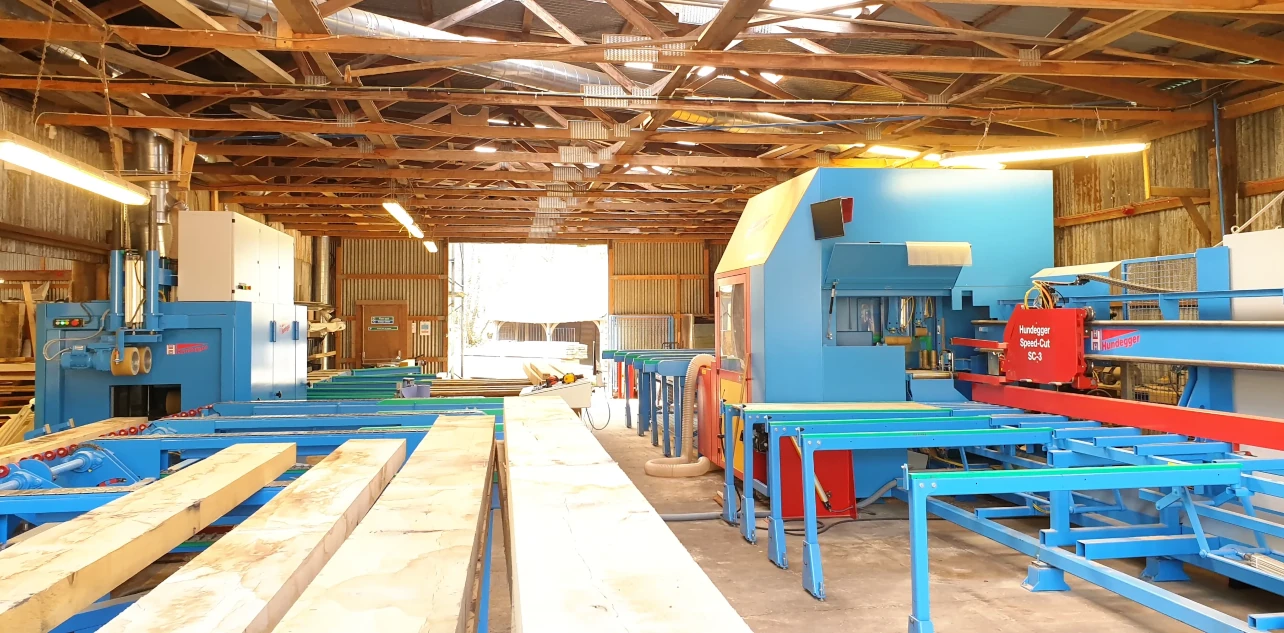 State-of-the-art oak frame manufacturing facility showing automated timber cutting line with Hundegger machine for crafting bespoke oak framed buildings and structures