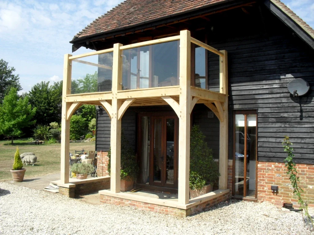 Oak Framed Balconies Freshly installed bespoke oak framed balcony with glass panels on a traditional black timber barn conversion in rural Berkshire featuring curved braces and clay tile roof