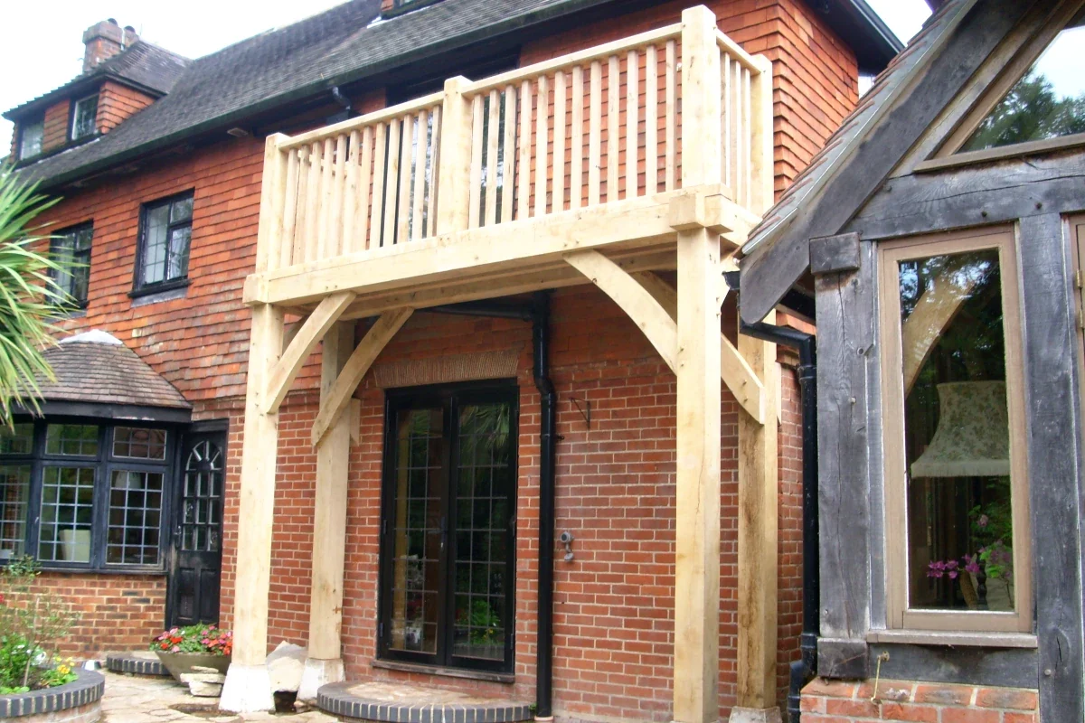 Oak Framed Balconies Bespoke oak framed balcony with timber balustrade on a traditional brick and tile-hung country house featuring curved braces and French doors in the Surrey Hills